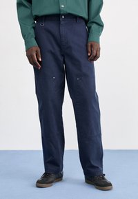 Mörk marinblå byxor med en avslappnad passform, tillverkade av bomull. Har framfickor, knäppning med knapp och synliga sömnadsdetaljer.