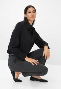 Schwarzes Hemd mit Knöpfen und Kragen, kombiniert mit dunkelgrauen, taillierten Hosen und schwarzen, spitzenBallerinas. Einfaches Design, glatte Textur, keine Muster.