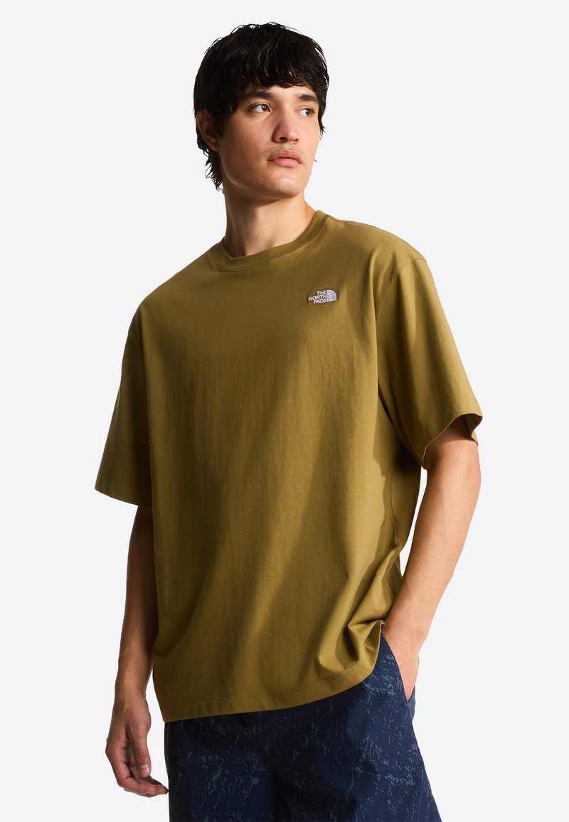 Oliwkowa bawełniana koszulka o luźnym kroju, z okrągłym dekoltem i logo The North Face na lewej piersi. Stylizowana z granatowymi, wzorzystymi szortami.