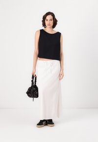 Top scurt negru, fustă maxi albă, adidași negri cu tălpi bej și un rucsac mic cu flori negre și șnur. Țesături netede și design simplu.