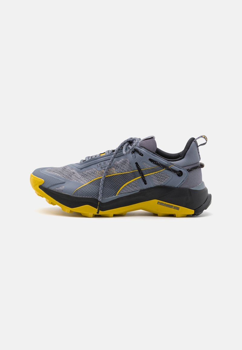 Zapatilla de trail running ligera en malla gris con acentos en negro y amarillo, que presenta una superficie texturizada y una suela resistente para tracción.