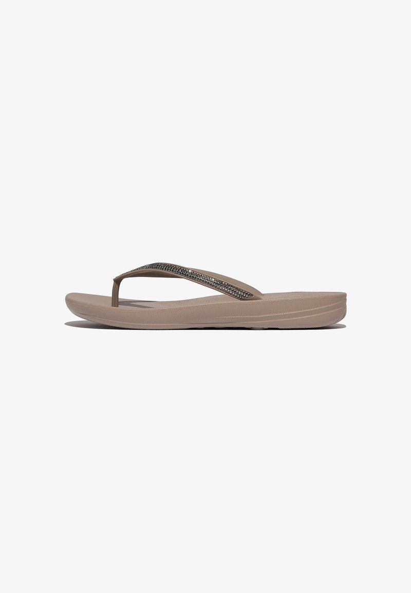 Tan flip-flops met een gestructureerde zool, voorzien van een transparante band versierd met kleine decoratieve elementen langs de bovenkant.