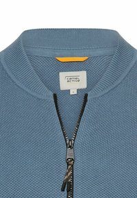 Blauer Reißverschluss-Pullover mit strukturiertem Strick, ausgestattet mit einem gerippten Kragen und einem Reißverschluss. Er hat einen kontrastierenden orangefarbenen Akzent unter dem Kragen.