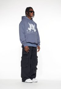 Hoodie i blå bomull med vit duvgrafik och texten "LOST YOU", ihopparad med svarta cargobyxor och vita sneakers.