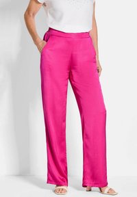 Satin roze broek met een wijde pijp, elastische tailleband en zijzakken. Draagt een witte top en lichtgekleurde sandalen.