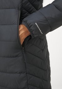 Crna padna jakna s quilted dizajnom, zatvorenim džepom i "OMNI-HEAT" brendiranjem na manžeti, koja prikazuje glatki, vodootporni materijal.