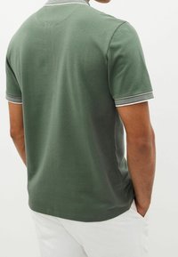 Tummanvihreä polo-paita, jossa on teksturoitu kangas, lyhyet hihat ja kontrastoiva valkoinen raidoitus kauluksessa ja hihojen reunoissa. Yksinkertainen ja slim fit -malli.