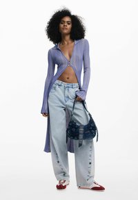 Világos lila bordázott zipzáros felső, magas gallérral, nyitott elülső résszel. Laza kék farmernadrág gombos részletekkel. Tengerészkék textúrájú kézitáska, piros-fehér sportcipő.