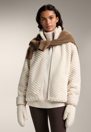Cream-colored fuzzy jacket with chevron texture, paired with a tan knitted scarf. Model wears beige sweater and light mittens.