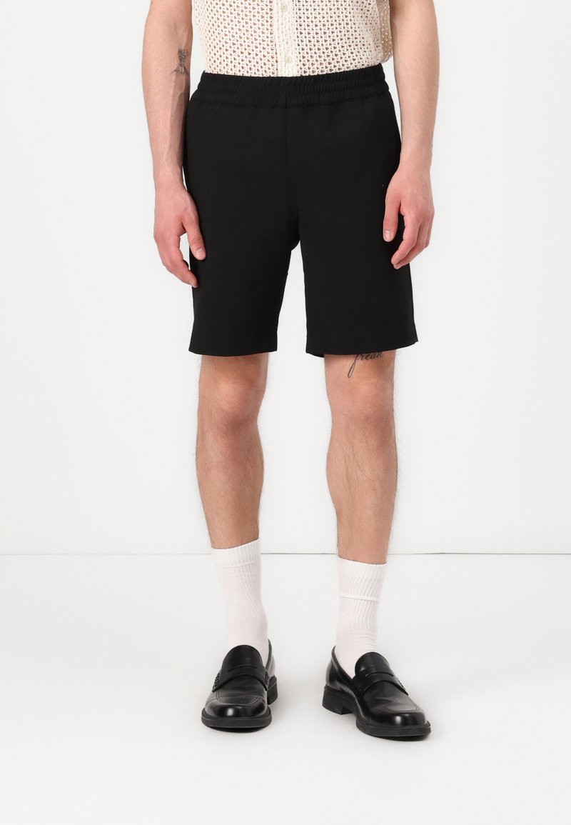Black elastic-waist shorts with a smooth texture, featuring a straight cut. Worn with white socks and black loafers.