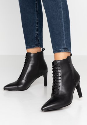 Bottes noires en cuir jusqu'à la cheville avec un bout pointu, un design à lacets et un talon aiguille de 7 cm. Texture lisse avec une subtile brillance.