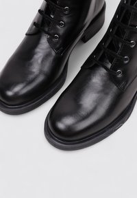 Bottines en cuir noir avec une finition lisse, doté d'un bout arrondi, d'un système de laçage et d'un petit talon en caoutchouc.
