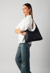 Black leather hobo bag with textured surface, gold hardware accents, and a curved shape. Worn over shoulder against a white background.