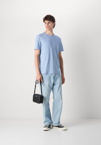 T-shirt ligeiramente azul de corte crew-neck, ajuste descontraído, combinado com jeans azul claro. Segurando uma pequena bolsa cruzada preta com uma alça de ombro.
