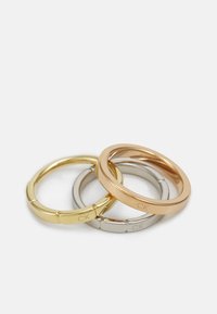 Set di tre anelli in tonalità oro, argento e oro rosa. Ognuno presenta un design liscio e arrotondato con dettaglio inciso del logo 'CK'.