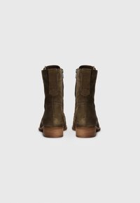 Paire de bottines en daim marron avec talons en bois et fermetures éclair visibles à l'arrière sur fond gris.