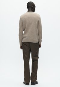 Beige strikket sweater med rund halsudskæring, ribstrikkede manchetter og kant. Kombineret med mørkebrune bukser og sorte sko.