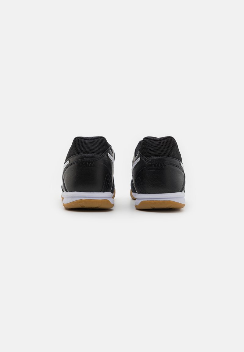 Des chaussures de sport noires avec une tige en cuir lisse, des panneaux en maille, des semelles blanches et une semelle extérieure en caoutchouc couleur gomme vues de l'arrière.