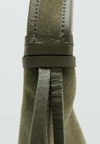 Sac à main en cuir et suède verts, présentant une surface texturée, une couture verticale et une forme épurée avec des accents en cuir.