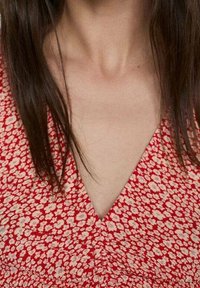 Vestido rojo con un estampado floral de pequeñas flores blancas, diseño de escote en V y una tela ligeramente texturizada.