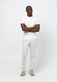 T-shirt blanc à col rond, pantalon crème ajusté et baskets beiges. Le tissu semble lisse avec un léger éclat. Pas de motifs ni d'accents.
