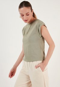 Oliven grøn kortærmet t-shirt med rund halsudskæring og afslappet pasform, lavet af blødt materiale; parret med lyse beige bukser.