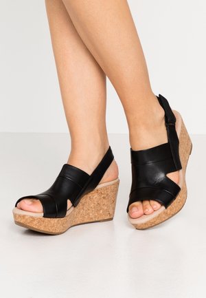Sorte læder kilehælssandaler med korkplatform, åben tå og ankelrem. Har udskæringer på siderne og en glat tekstur.