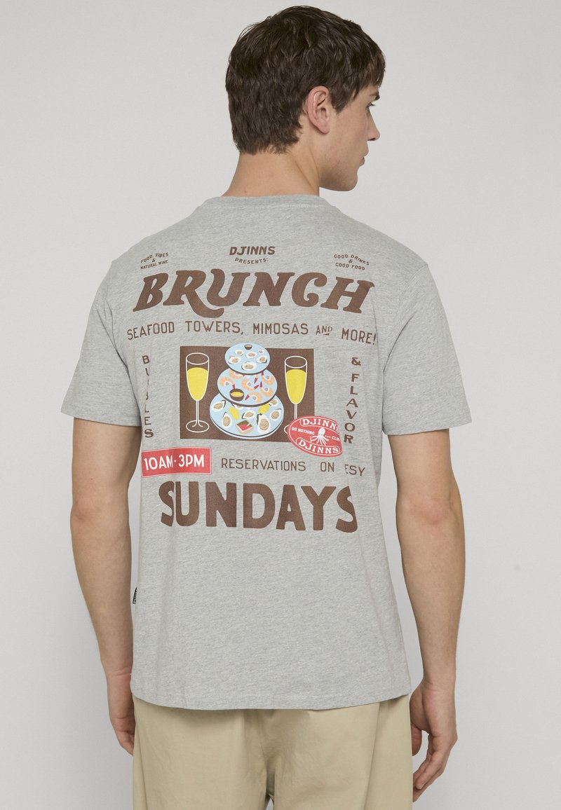 Man wearing gray t-shirt with brunch-themed graphic showing seafood towers, mimosas, and Sunday reservation times on the back.