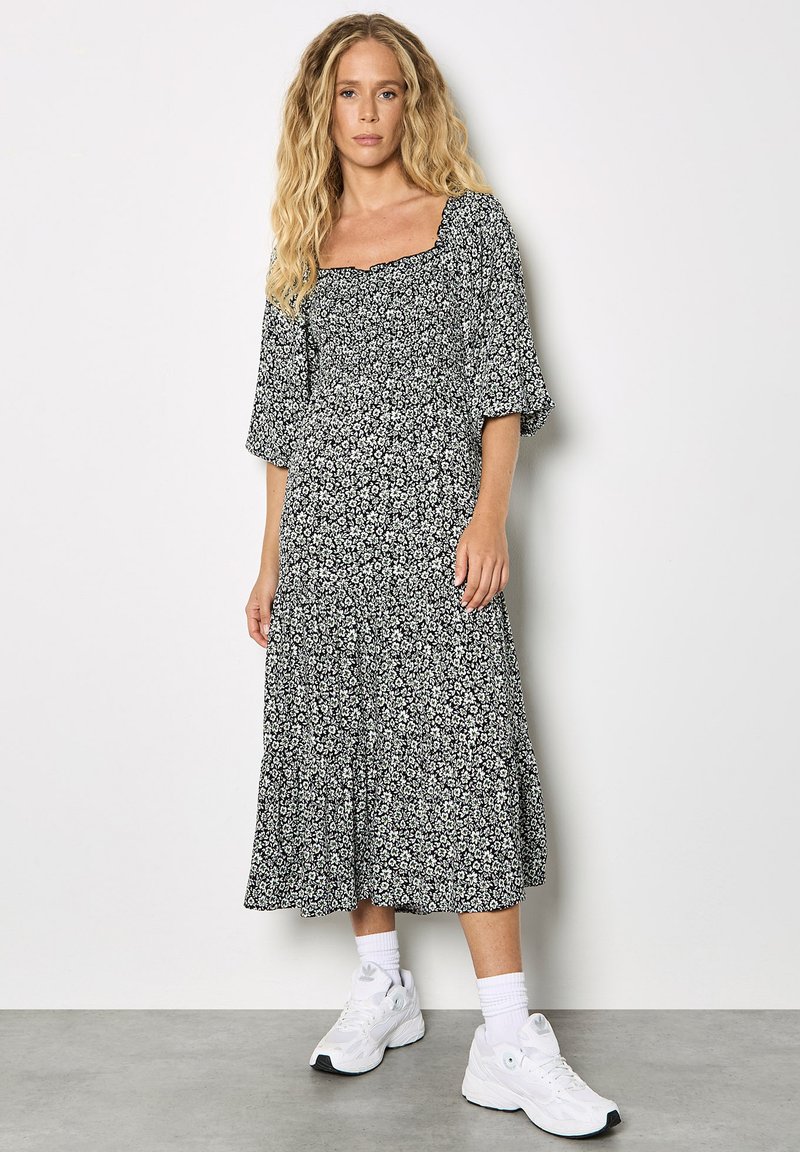 Vestido midi negro con estampado floral, escote cuadrado, bajo con volantes en capas y mangas acampanadas, combinado con zapatillas blancas y calcetines hasta la pantorrilla.