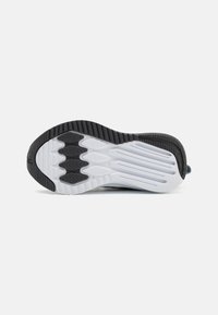 Semelle de chaussure de sport en noir et blanc avec un motif de grip texturé ; présente des stries et des rainures flexibles pour la flexibilité et la traction.