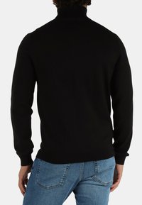 Maglione nero in maglia con collo alto e maniche lunghe, caratterizzato da una trama a coste, abbinato a jeans in denim blu chiaro.
