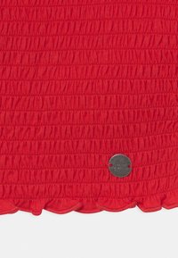 Czerwony marszczony materiał z małą falbaną u dołu oraz metalową metką z napisem "Love Jeans". Gładka faktura.