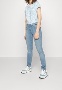 Camisa de estampado azul claro con mangas cortas, combinada con jeans ajustados azul claro y zapatillas gris-azul con acentos blancos.