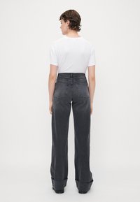 Jeans a vita alta e gamba larga in denim grigio scuro, con cuciture a contrasto, due tasche posteriori e una maglietta bianca casual.