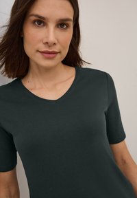 T-shirt à manches courtes de couleur vert foncé avec un design à col en V. Fabriqué en tissu doux avec une texture lisse, présentant une coupe décontractée.