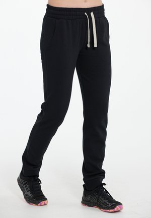 Sorte sweatpants med elastisk talje og snoretræk, med sidelommer og tapered ben. Båret med sorte sportssko.