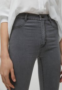 Jeans de mezclilla gris ajustados con cintura alta, que presentan un cierre delantero, diseño de cinco bolsillos y sutiles detalles de costura.