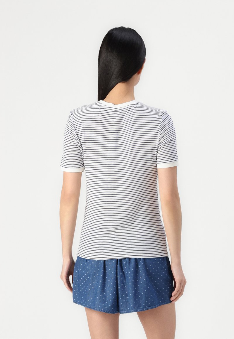 Gestreiftes T-Shirt mit kurzen Ärmeln, weißem Grund und dunkelblauen Streifen, mit Rundhalsausschnitt und figurnahem Schnitt; kombiniert mit blauen Shorts mit Punkten.