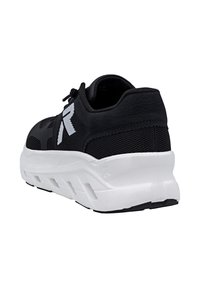 Scarpa sportiva nera con suola spessa bianca, dettagli in rete e un grande logo bianco "R" sul lato, mostrata da un'angolazione posteriore.