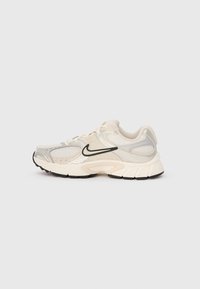 Világos bézs és fehér Nike futócipő, hálós panelek, fekete swoosh logó és vastag párnázott talp, egy sima háttér előtt.