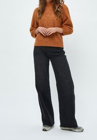 Suéter de punto color óxido con textura acanalada, combinado con unos pantalones vaqueros de pierna ancha de cintura alta en negro y zapatillas gris.