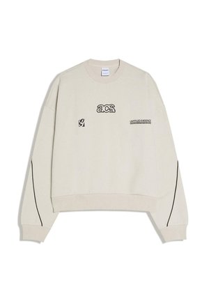 Krémová mikina s čiernym nápisom "acs." a "UNTITLED EVIDENCE" na prednej strane, čierne pruhy pozdĺž rukávov, rebrované manžety a lem.