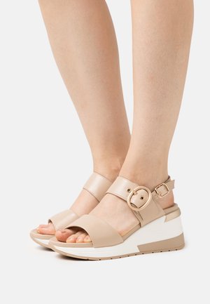 Beige kile sandaler har en glat læderoverdel med en bred rem, ankelspænde og en kontrasterende hvid sål med et tekstureret greb.