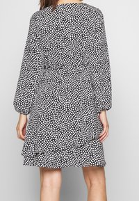 Black dress with a white abstract pattern, long sleeves, gathered waist, and layered ruffle hem, made from lightweight fabric.