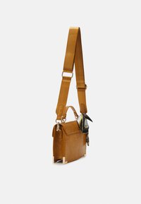 Sac à bandoulière en cuir synthétique marron effet crocodile avec une large sangle réglable et un foulard décoratif noir et blanc attaché à la poignée.