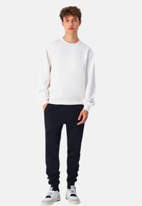 Sudadera de algodón blanca, con puños acanalados, combinada con joggers negros y zapatillas blancas, que presenta un diseño sencillo y un ajuste relajado.