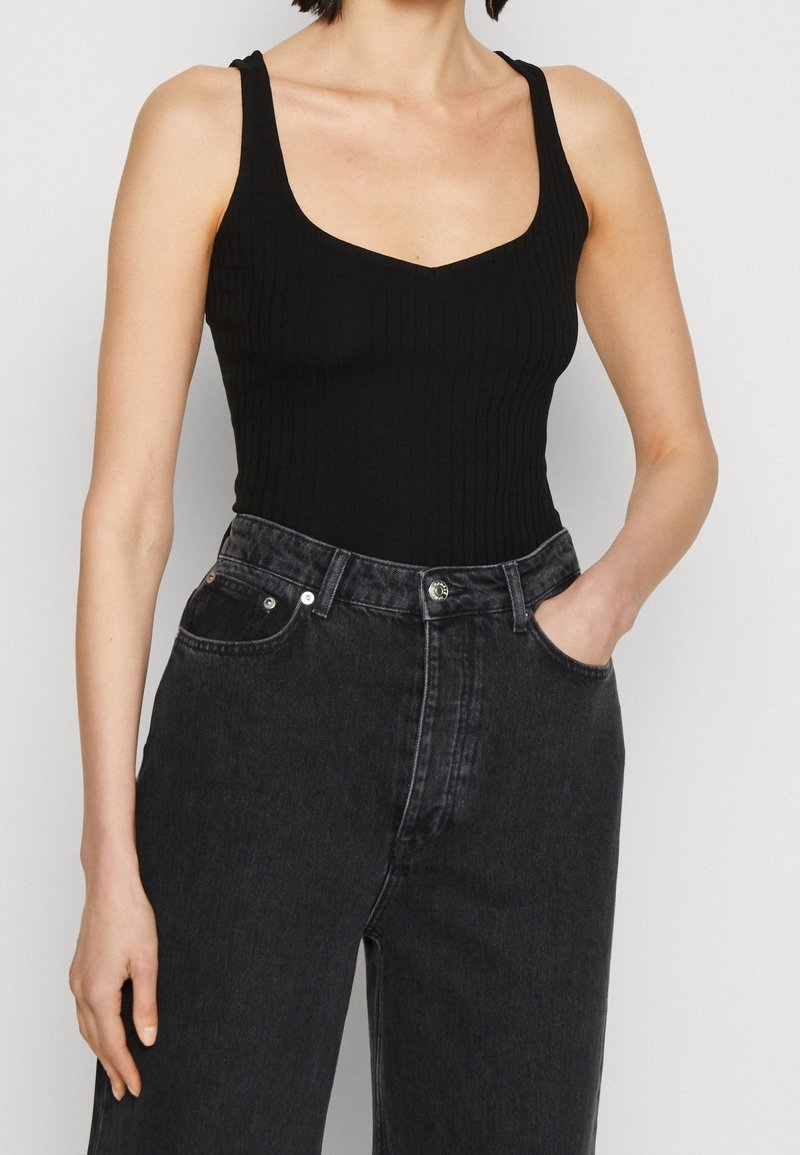 Černý žebrovaný body s širokými ramínky a čtvercovým výstřihem, v kombinaci s černými džínami se zvýšeným pasem a klasickým pětipocket designem.