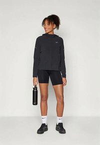 Schwarze Sportjacke mit Kapuze, kombiniert mit schwarzen Shorts. Das Outfit beinhaltet schwarze Sneakers und eine Wasserflasche aus Edelstahl.