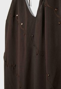 Tissu marron foncé avec une délicate broderie en feston et de petites paillettes disposées en un motif ondulé sur un vêtement.