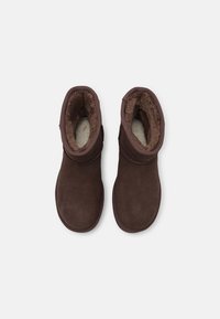 Paire de bottines en daim marron avec doublure en fourrure moelleuse, vues du dessus sur fond blanc.